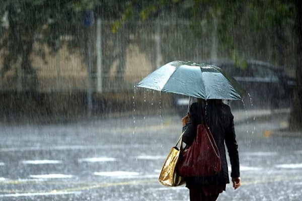 Mulher segurando guarda-chuva enquanto atravessa uma via molhada
