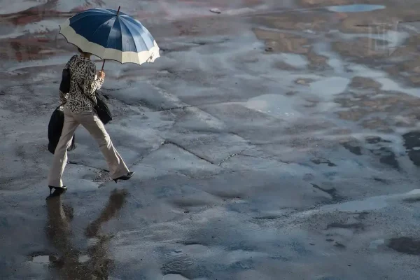 Mulher caminha com guarda-chuva na mão direita