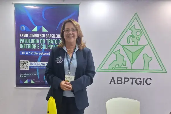 Foto da Dra. Carmem Luiza Leite, presidente do Congresso e da ABPTGIC-SE, com o poster do XXVIII Congresso Brasileiro de Patologia do Trato Genital Inferior e Colposcopia (PTGIC), no seu lado direito
